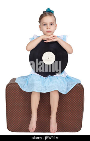 Das kleine Mädchen sitzt mit einer Vinyl-Schallplatte auf einem alten Koffer Stockfoto