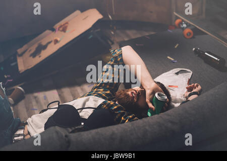 Betrunken bärtiger junger Mann schlafend auf der Couch mit BH und Bier kann nach party Stockfoto