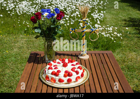 Tabelle mit Erdbeerkuchen und Dekorationen in einem Garten mit wachsenden Gänseblümchen Stockfoto