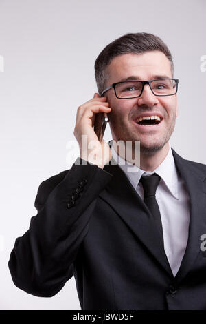 ein eleganter gekleidet Mann mit einer Brille glücklich und sein Handy im Gespräch Stockfoto