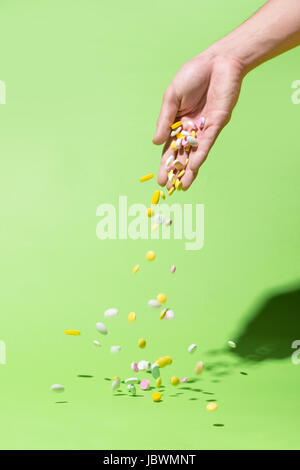 Farbigen Pillen fallen von Hand auf grünem Hintergrund. Stockfoto