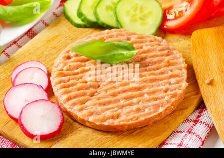 Rohe Burger Patty und geschnittene Gemüse auf Schneidebrett Stockfoto