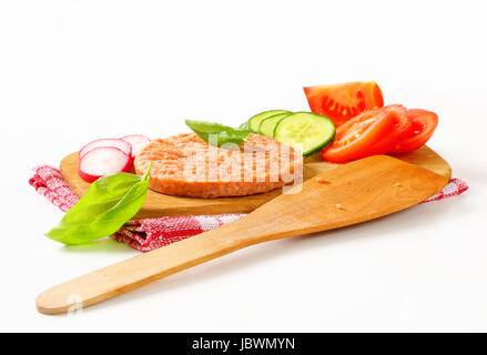 Rohe Burger Patty und geschnittene Gemüse auf Schneidebrett Stockfoto