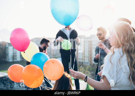 Gruppe von Freunden genießen Dach Partei, junge Frau, die mit Helium-Ballons Stockfoto