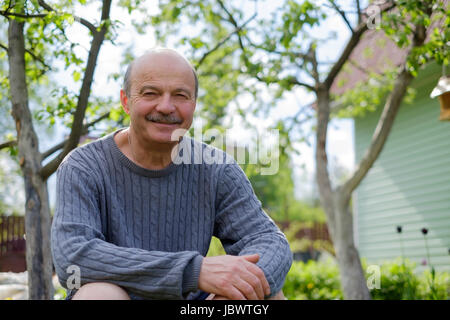 Reifer Mann sitzen im Garten in der Nähe von Apfelbaum im Land Stockfoto