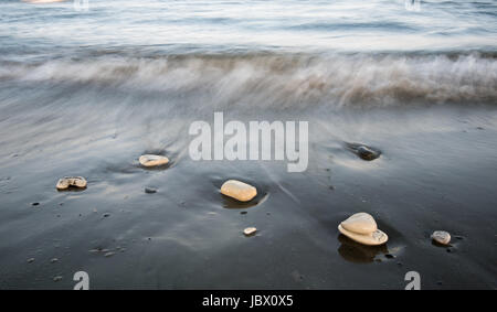 Kieselsteine am Strand auf einem schwarzen Sand und fließt Meerwasser schöne Texturen erstellen. Langzeitbelichtung Bild. Stockfoto