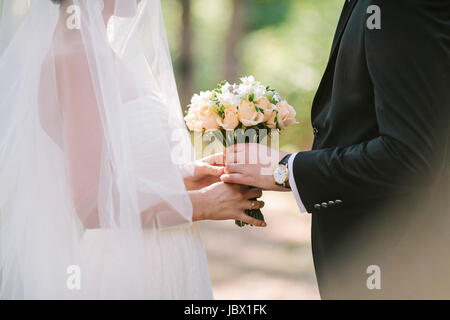 der Bräutigam gibt der Braut einen Hochzeitsstrauß im Freien. Stockfoto