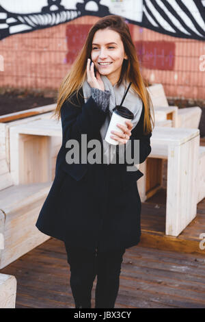 Glückliche junge Teenager Frau am Telefon Lachen mit einer Tasse Kaffee zum mitnehmen Stockfoto