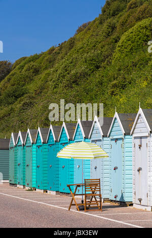 Tisch, Stuhl und Sonnenschirm außerhalb Strandhütten in Schattierungen von Türkis Blau Grün in Bournemouth im Juni Stockfoto