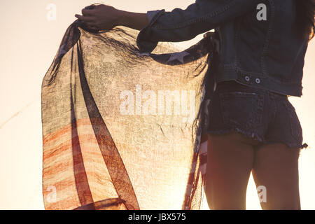 Woman wearing denim shorts, holding American flag, mid section, rear view Stockfoto