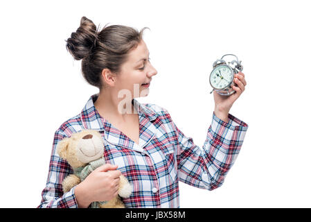 Mädchen im Schlafanzug auf Wecker und sieht in der hand einen Teddybär auf weißem Hintergrund Stockfoto