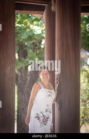 Brünette Frau mittleren Alters, zu Fuß durch den Korridor mit Holzsäulen. Stockfoto