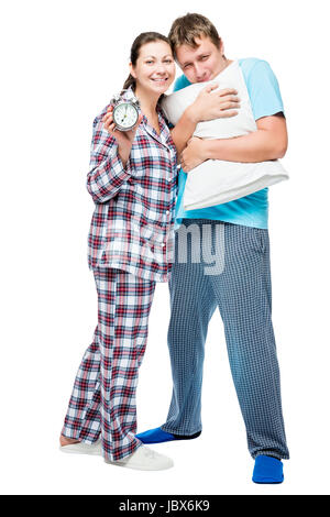 Junges Paar im Pyjama mit Kissen und Wecker auf weißem Hintergrund posiert