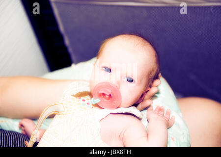 Schön wach Baby Girl saugt an einem Schnuller auf Mutters Schoß liegend Stockfoto