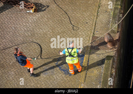 Hafenarbeiter anbringen vertäut Schiffs Trosse Shoreside Bitt auf Kai im Hafen dock Stockfoto