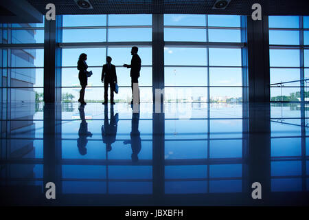 Silhouetten von mehreren Büroangestellte am Fenster stehen und reden Stockfoto