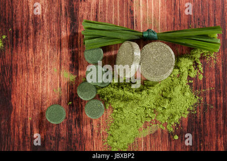 Gerste, Weizengras, Spirulina und Chlorella grass Pillen, Grashalme und Boden Pulver auf braunem Holz Hintergrund, Ansicht von oben. Detox. Stockfoto