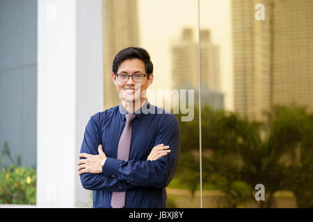 Porträt des chinesischen Geschäftsmann stand mit verschränkten in der Nähe von Bürogebäude in Panama. Reflexionen der Stadt am Spiegel Stockfoto