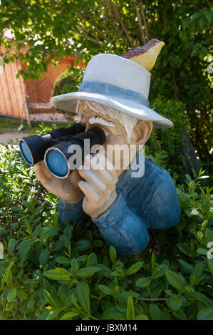 Menschliche Figur mit Vogel am Hut und Fernglas, mit Blick auf eine Hecke, Bayern, Deutschland Stockfoto