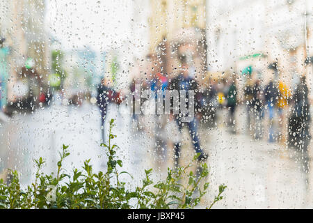 Zusammenfassung Hintergrund unscharf junger Menschen zu Fuß die Straße hinunter in regnerischen Tag. Regentropfen auf Fensterglas. Vorsätzliche Bewegungsunschärfe. Konzept der modernen urbanen lifestyle Stockfoto