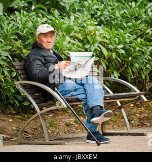 Quadratische Porträt eines alten Mannes lesen der Renn-Seiten in Hong Kong, China. Stockfoto