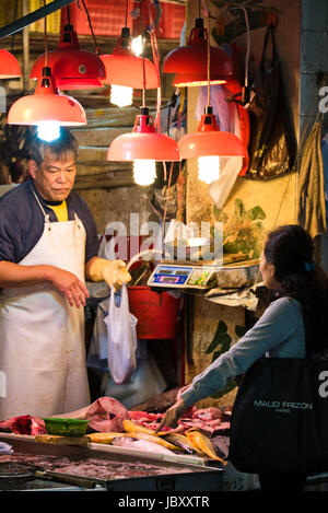 Vertikale Porträt eines Kunden kaufen Fisch bei einem Fischhändler Stand auf dem nassen Markt in Hong Kong, China. Stockfoto