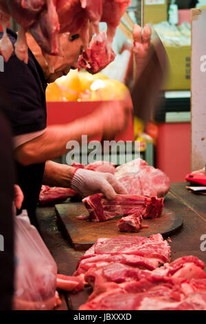 Vertikales Porträt eines Metzgers, der Fleischstücke auf einem feuchten Markt in Hongkong, China, hackt. Stockfoto