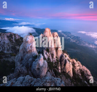 Berglandschaft bei Sonnenuntergang. Blick vom Gipfel auf hohen Felsen, blauer Himmel, rote Wolken und Meer am Abend. Niedrige Wolken. Bunte nat Stockfoto