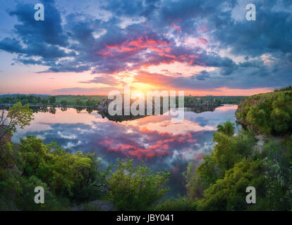 Wunderschöne Szene mit Fluss, grüne Bäume, Felsen und erstaunlich blauen Himmel mit bunten Wolken spiegeln sich in Wasser bei Sonnenuntergang. Fantastische Sommerlandschaft mit Stockfoto