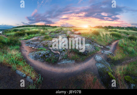 Bunte Sommerlandschaft mit großen Steinen, grasgrün, Gehweg und erstaunlichen Himmel mit bunten Wolken bei Sonnenuntergang. Natur-Hintergrund. Felsen in der sein Stockfoto