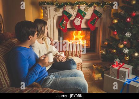 Schöne junge Frau und Mann Entspannung durch den Kamin und geschmückter Weihnachtsbaum Stockfoto