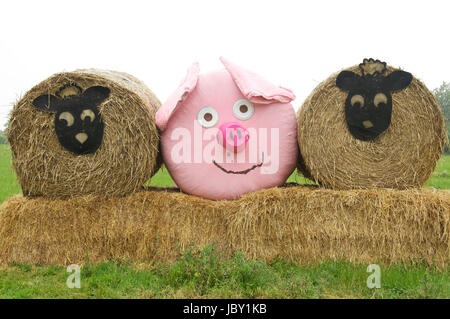 Comic-Tiergesichtern Vertretung Schafe und ein rosa Schwein schmücken drei Heuballen, angeordnet in einem Feld in der Nähe von Dorchester. Dorset, England, Vereinigtes Königreich. Stockfoto