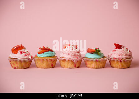 Frisch gebackene bunten Cupcakes dekoriert mit Streuseln und Erdbeeren auf rosa Hintergrund Stockfoto