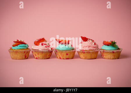 Nahaufnahme Foto Reihe von rosa und blaue Cupcakes mit frischen Erdbeeren auf rosa Hintergrund Stockfoto