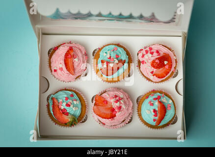 Blick von oben auf schöne bunte Cupcakes mit Streuseln und Erdbeere im Feld Stockfoto