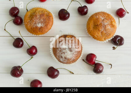 Drei frisch gebackene Muffins und Kirschen auf weißer Holztisch Stockfoto