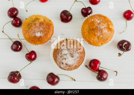 Draufsicht auf drei Muffins mit Kirschen auf weißem Holz Schreibtisch Stockfoto