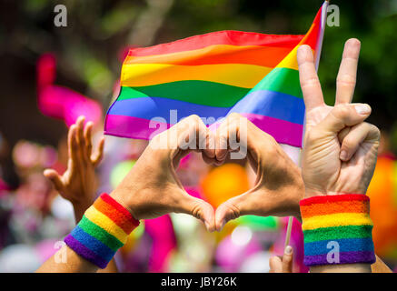 Unterstützende Hände machen Frieden und Herz-Zeichen vor der einen Regenbogenflagge am Rande einer Sommer-gay-Pride-parade Stockfoto