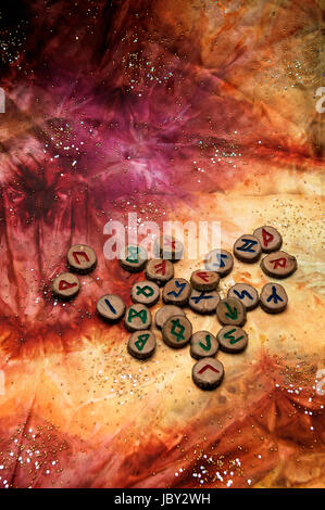 Hand geschnitzt und bemalt aus Holz Runen, eine antike Alphabet das Futhark genannt sind auf eine bunte Hand gefärbtes Gewebe mit kleinen funkelnden Perlen. Hinweis: Diese Runen wurden von den Fotografen gemacht. Stockfoto