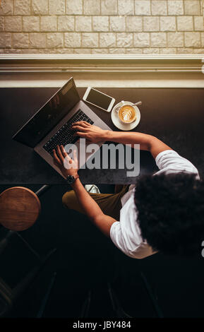 Draufsicht der junge Mann im Café sitzen und arbeiten am Laptop. Vertikale Overhead Schuss von Mann mit Laptop im Café. Stockfoto