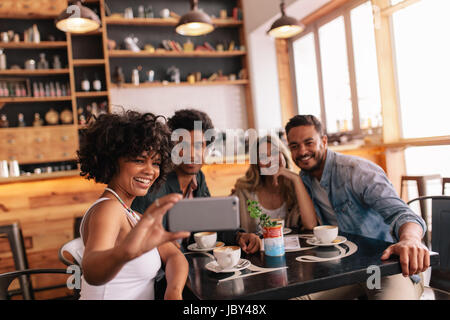 Gemischtrassige Leute, die Spaß im Café ein Selbstporträt mit Handy nehmen. Gruppe junger Freunde sitzen im Restaurant unter Selbstporträt mit smart Stockfoto