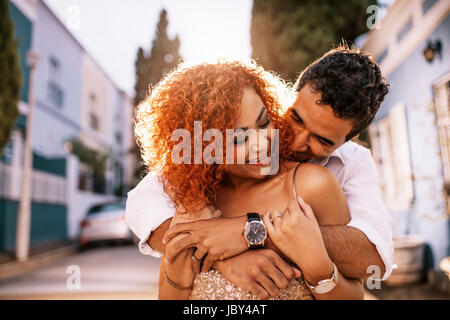Mann in gute Laune, die Frau in die Arme von hinten zu halten, während die Frau in seinen Händen hält. Lächelnde Frau genießen die Gesellschaft von ihrem Partner. Stockfoto
