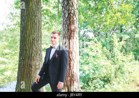 Elegante Bräutigam im schwarzen Kostüm und lila Fliege. Bräutigam am Tag seiner Hochzeit. Wunderschönen lächelnden Bräutigam im Freien. Stockfoto