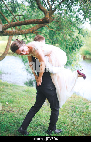 Porträt von ein hübscher junger Mann mit attraktiven Frau auf dem Rücken im Freien. Spaß paar. Braut und Bräutigam Stockfoto