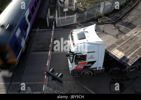 Mercedes-Benz Actros Lkw ziehen einen leeren Tieflader wartet darauf, dass ein Zug auf einem Bahnübergang in Rotherham, South Yorkshire übergeben Stockfoto