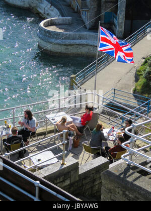 Menschen sitzen im Terrassencafé auf Plymouth Hacke Erfrischungen an sonnigen Sommertag neben Tinside Pool genießen. Sonne glitzern des klaren, blauen Meerwasser Stockfoto