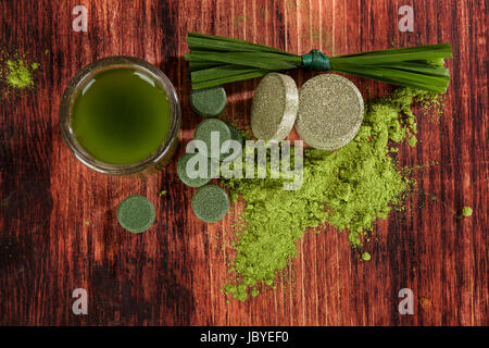 Detox. Grüne Lebensmittel ergänzt Chlorella, Weizen Grass und Spirulina Tabletten, Grundpuder, Grashalme und grüne Getränk auf braunem Holz Hintergrund, Ansicht von oben. Stockfoto