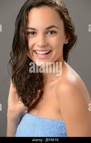 Teenager-Mädchen Touch nasses Haar Pflege lächelnde Brünette auf grauem Hintergrund Stockfoto