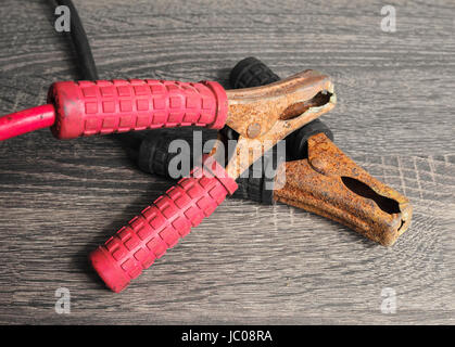 Jumper-Kabel zum Aufladen der Autobatterie. Rot und schwarz, negative und positive Kabel auf einem hölzernen Hintergrund. Stockfoto