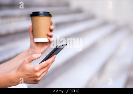 Nahaufnahme von eine Geschäftsfrau mit Handy und Pappbecher halten. Nahaufnahme Detail einer Geschäftsfrau Hand hält Pappbecher und per smartphone Stockfoto